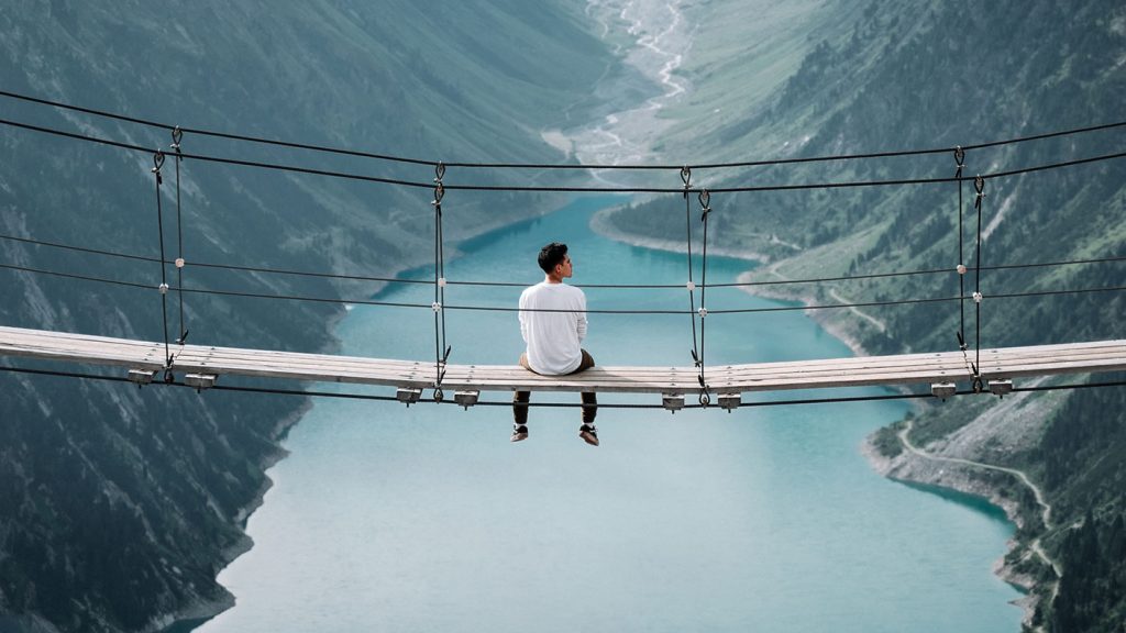 Man sitting on a bridge overlooking a beautiful canyon landscape